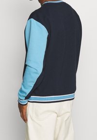 Men's color-blocked sweatshirt in navy and light blue, featuring a ribbed collar and cuffs, with striped detailing at the hem.