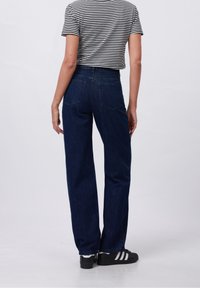 Vaqueros de mezclilla azul oscuro de tiro alto con pierna recta, bolsillos traseros y una camiseta a rayas casual. El conjunto se completa con zapatillas negras.