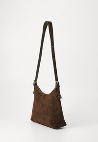 Braune Wildleder-Schultertasche mit verstellbarem Trageriemen und silbernen Schnallen-Details, leicht trapezförmige Form, Reißverschluss oben.