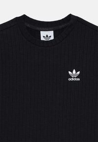 Črn rebrast pulover s okroglim izrezom, ki ima na prsih belo logo Adidas in teksturirano tkanino.