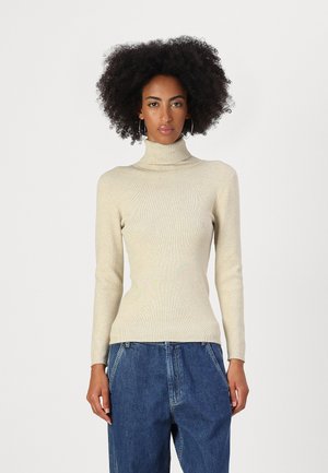Beige ribbed turtleneck sweater with long sleeves, form-fitting design, and a smooth texture, paired with loose blue denim pants.