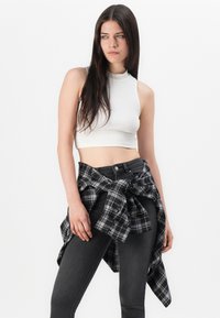 Valkoinen ribatu crop-top, yhdistettynä mustiin korkeavyötäröisiin skinny-farkkuihin, joissa on musta-harmaata ruudullinen paita sidottuna vyötärölle.