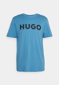 Niebieska koszulka z krótkim rękawem i okrągłym dekoltem z czarnym tekstem "HUGO" napisanym dużymi literami na klatce piersiowej.