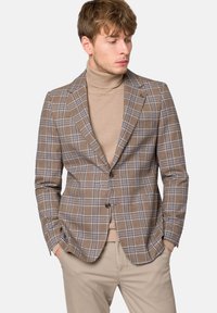 Brązowa marynarka w kratę z niebieskimi akcentami, dopasowany krój, jedno guziki z zapięciem oraz klapy w szpic, zestawiona z beżowym swetrem z golfem.