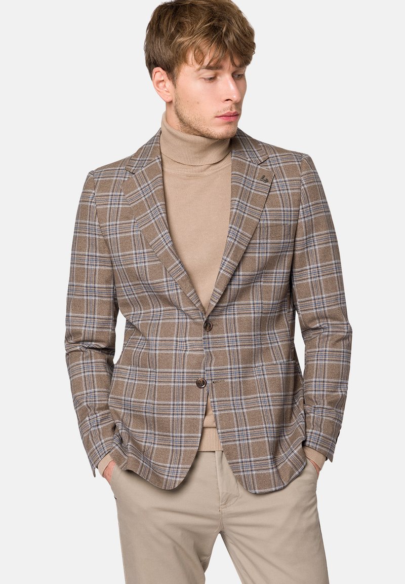 Brązowa marynarka w kratę z niebieskimi akcentami, dopasowany krój, jedno guziki z zapięciem oraz klapy w szpic, zestawiona z beżowym swetrem z golfem.