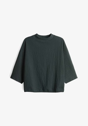 Maglione lungo a maniche lunghe di un verde scuro con collo rotondo e vestibilità ampia, disteso su uno sfondo bianco.