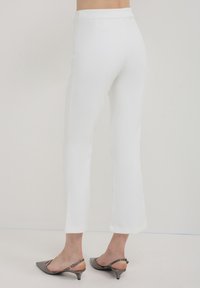 Pantalon tailleur blanc avec une finition lisse, design à jambe droite et taille mi-haute. Associé à des escarpins gris à bride arrière.