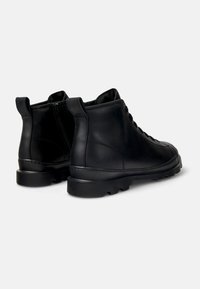 Botas de tobillo de cuero negro con un exterior suave, puntera redondeada, cordones en la parte delantera y suela de goma texturizada con un diseño de tacos definido.