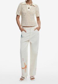 Top in maglia con base crema, maniche corte e due grandi bottoni. Pantaloni bianchi a vestibilità ampia con motivi ricamati a tema marino e tasche.