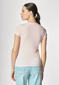 T-shirt aderente rosa chiaro con maniche corte, scollatura rotonda e texture liscia, abbinato a jeans azzurri chiari con tasche posteriori.