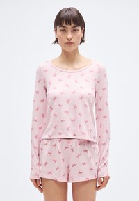 Σετ πιτζάμες σε ροζ χρώμα που περιλαμβάνει μπλούζα με μακριά μανίκια και σορτς, και τα δύο με μικρά μοτίβα φιόγκων. Μαλακό ύφασμα με άνετη εφαρμογή και ελαστική μέση.