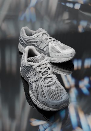 Pair of gray New Balance running shoes with mesh uppers and white laces resting on a reflective dark surface.