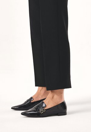 Sorte patenterede loafers med spidse tæer, der har vandrette folder og guldspænder. Skoene har en lav, flad hæl.