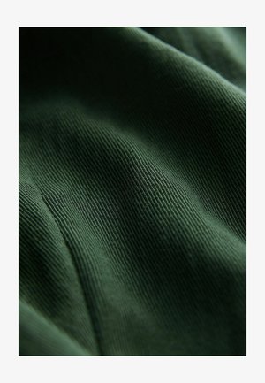 Mörkgrön ribbad tyg med subtil textur och stretch. Materialet visar fina linjer som löper horisontellt över ytan.