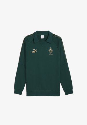 Ciemnozielony sweter z kołnierzykiem, z długimi rękawami. Złote detale z logo zawierają napis "KING" oraz kształt diamentu z napisem "125 Jahre". Wzorzyste akcenty na ramionach.