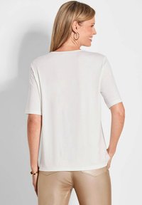 Witte top met korte mouwen en een ontspannen pasvorm, een gladde textuur en een rechte zoom, gecombineerd met glanzende, strakke beige broek.