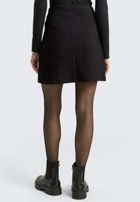 Fekete textúrájú mini szoknya, formás derékkal, sima felülettel. Opak fekete harisnyával és csuklós csizmával párosítva.