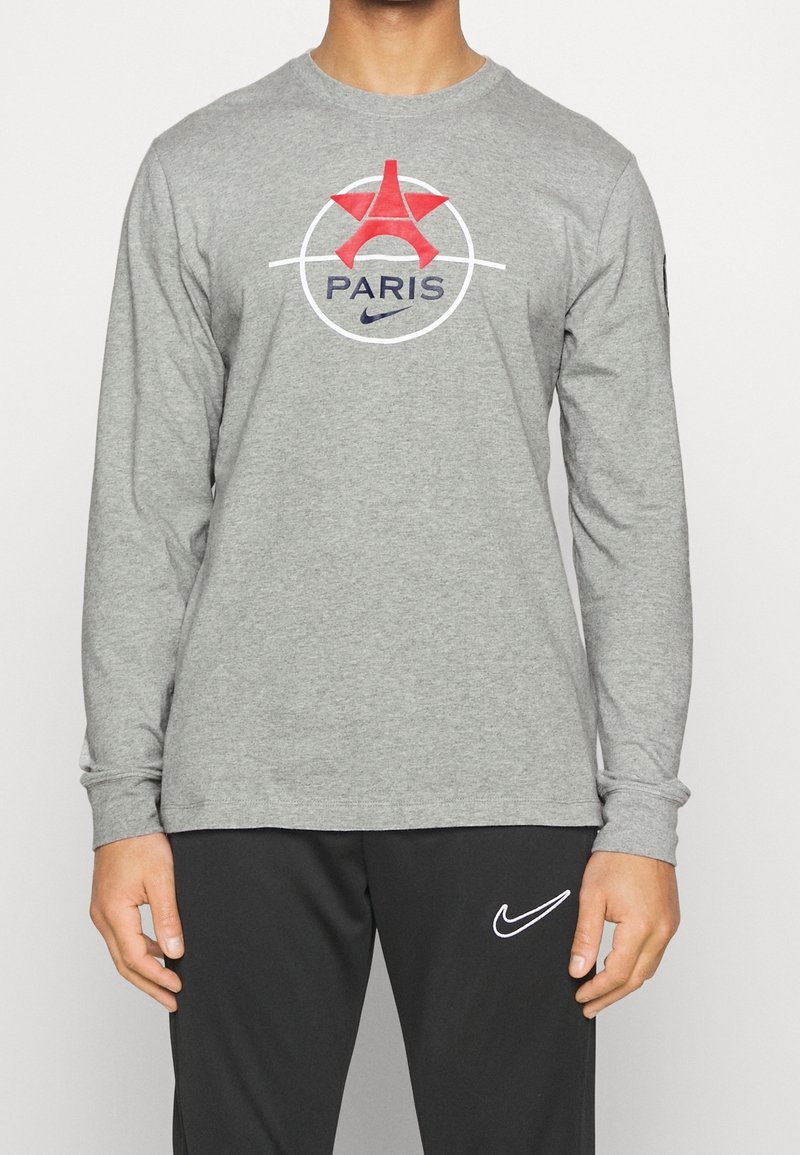 Graues Langarm-T-Shirt mit einem Grafikdesign des Eiffelturms und "PARIS" in Blau, umrandet von einem weißen Kreis und mit dem Nike-Logo.