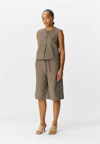 Bruine, mouwloze top met knopen aan de voorkant, gecombineerd met bijpassende kniebakke shorts. Soepele stof, minimalistisch ontwerp en relaxte pasvorm.