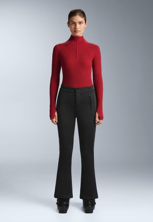 Rdeča rebrasta majica z visokim ovratnikom in polovičnim zadrgo, združena z visokim črnim razširjenim hlačam s stranskimi žepki z zadrgo in gladko teksturo.