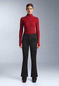Röd ribbad polotröja med halv dragkedja, kombinerad med högmidjade svarta utsvängda byxor med sidofickor med dragkedja och en mjuk textur.