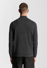 Donkergrijze gebreide trui met een rechte snit en lange mouwen. Heeft een hoge kraag en ribgebreide boorden en zoom. Minimalistisch ontwerp.