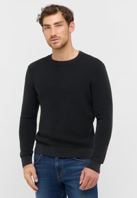 Pull noir à côtes avec un col rond et des manches longues, fabriqué en tissu texturé, associé à un jean bleu.