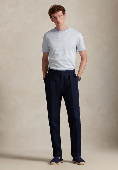 Ανοιχτό μπλε ριγωτό μπλουζάκι με στρογγυλή λαιμόκοψη, συνδυασμένο με ναυτικό μπλε παντελόνι με πτυχώσεις. Τα παπούτσια είναι ναυτικά μπλε εσπαντρίγιες με σόλα από σχοινί.