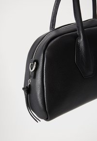 Bolsa de mão em couro preto com acabamento texturizado. Possui um zíper e ferragens prateadas, formato arredondado e alças curtas.