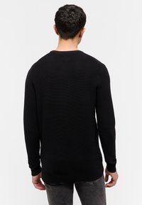 Schwarzer gestrickter Pullover mit Rundhalsausschnitt, langen Ärmeln und gerippten Bündchen. Die Textur ist glatt mit einem dezenten Muster.