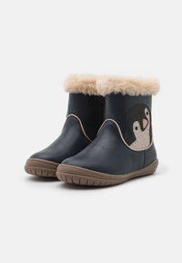 Botas azul marino con un ribete de piel sintética, que presentan un diseño de pingüino en un panel lateral texturizado y una suela de goma flexible de color marrón.