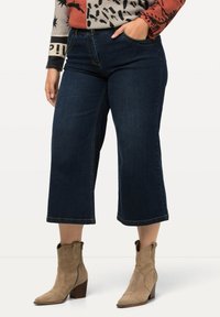 Tmavě modré džínové culotte kalhoty s polovičním pasem, které mají klasický design s pěti kapsami a viditelnými švy.