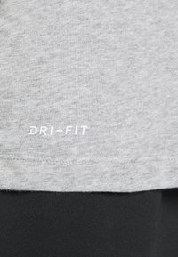 Tessuto DRI-FIT grigio con una texture morbida, caratterizzato da un logo bianco vicino all'orlo, abbinato a leggings sportivi neri.