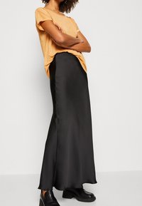 Zwarte satijnen maxi rok gecombineerd met een metallic gouden top met korte mouwen, voorzien van een relaxte pasvorm. Schoeisel bestaat uit zwarte schoenen met een dikke hak.