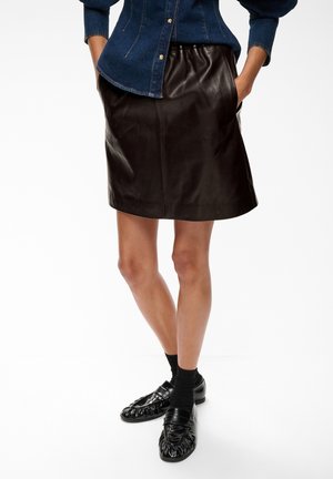 Personne portant une jupe en cuir noire, des chaussettes noires et des mocassins noirs avec une chemise en denim bleue rentrée à la taille.