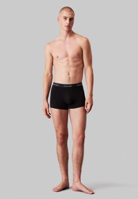 Boxers ajustados de algodón negro con una amplia cinturilla elástica que presenta el logo de "Calvin Klein". Textura suave, diseño ajustado.