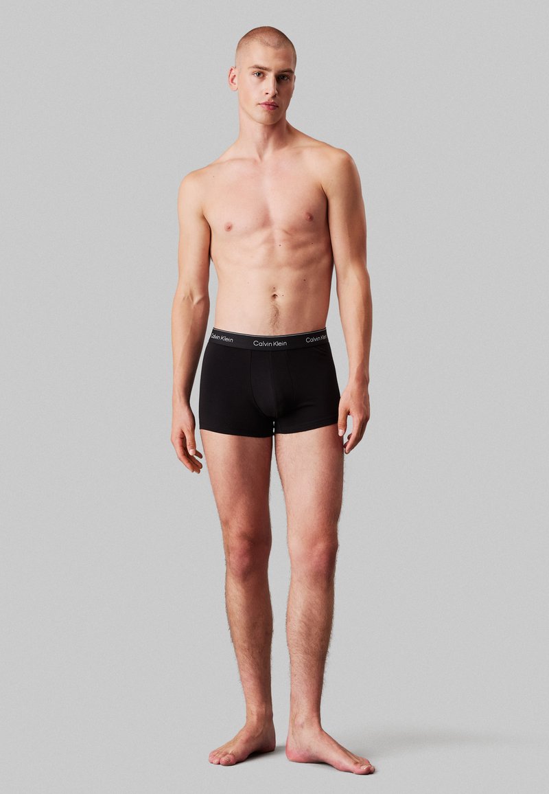Boxers ajustados de algodón negro con una amplia cinturilla elástica que presenta el logo de "Calvin Klein". Textura suave, diseño ajustado.