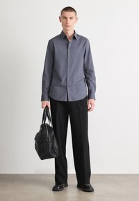 Γκρι πουκάμισο με λείο υλικό, σε συνδυασμό με μαύρο παντελόνι ευρείας γραμμής και μαύρη δερμάτινη τσάντα, που περιλαμβάνει μινιμαλιστικά σχεδιαστικά στοιχεία.