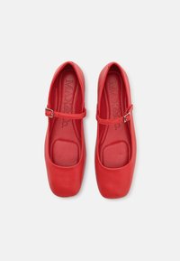 Bailarinas de cuero rojo con una forma de punta redonda y una pequeña correa ajustable. Textura suave y plantilla acolchada visibles.