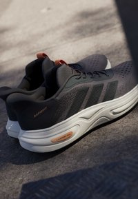 Ein Paar dunkelgraue Adidas Laufschuhe mit weißen Sohlen auf Beton, mit den Beschriftungen „RAPIDFIT“ und „CLOUDFOAM“.
