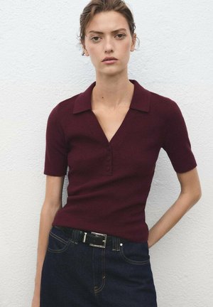 Burgundy short-sleeve top with a V-neck and three buttons, paired with a dark denim skirt. Smooth knit texture, casual design.