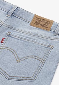 Hellblaue Jeans aus Denim mit einem braunen Lederetikett. Verfügt über kontrastierende goldene Nähte und ein markantes Design der Gesäßtaschen.