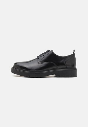 Black leather dress shoe with a smooth finish, round toe, and low, textured sole. Features lace-up design and heel tab for easy wear.