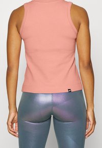 Jasnoróżowy top bez rękawów z teksturowanego materiału, w połączeniu z błyszczącymi, dopasowanymi legginsami w odcieniu teal, które mają odbijający blask.