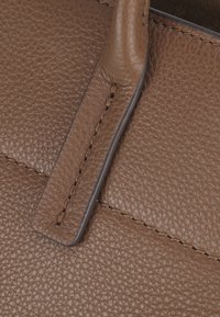 Textures in pelle marrone con una finitura a ciottoli, caratterizzata da una maniglia liscia e da una cucitura intricata lungo i bordi.