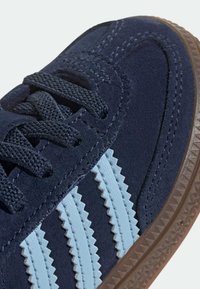 Námořnicky modrá semišová teniska s světle modrými cikcak pruhy, texturovanými tkaničkami a gumovou podrážkou s vzorovaným okrajem.