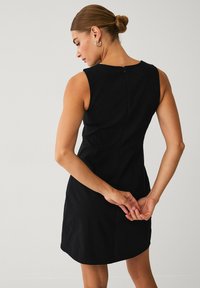 Sort ærmeløs kjole med skræddersyet pasform, lynlås bagpå, glat tekstur og knælængde. Elegant design med minimal detaljering.