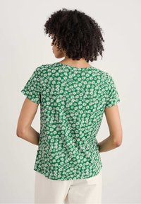 Top verde a maniche corte con stampa di margherite. Tessuto morbido, colletto rotondo, vestibilità comoda e orlo leggermente curvato.
