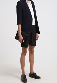 Námořnický blejzr, bílá košile s květinovými akcenty, černé kraťasy a černé šněrovací boty. Kapsička v ruce, hladké textury.