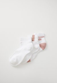 Chaussettes en coton blanc avec des accents roses. Longueur courte, bords côtelés. Présente une étiquette de logo et un branding subtil sur le côté.